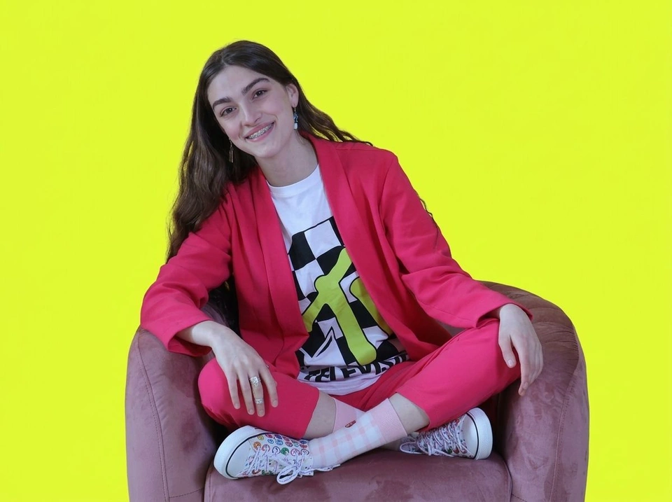 Smiling woman in a pink suit seated against a lime background